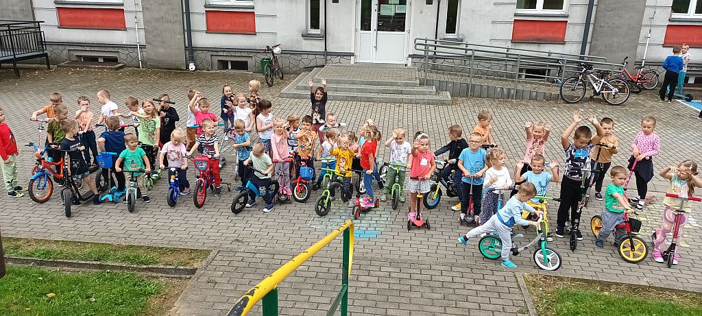 Grupa dzieci przed szkoła z rowerami i hulajnogami
